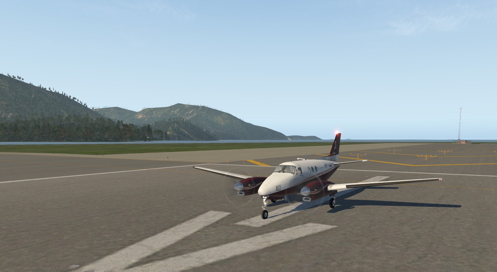 In this image you see a photo of the Beechcraft King Air Airplane from X-Plane 11 sitting on the tarmac with mountains in the background.